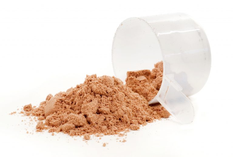 Chocolate protein powder spilling from a clear scoop on a white surface.